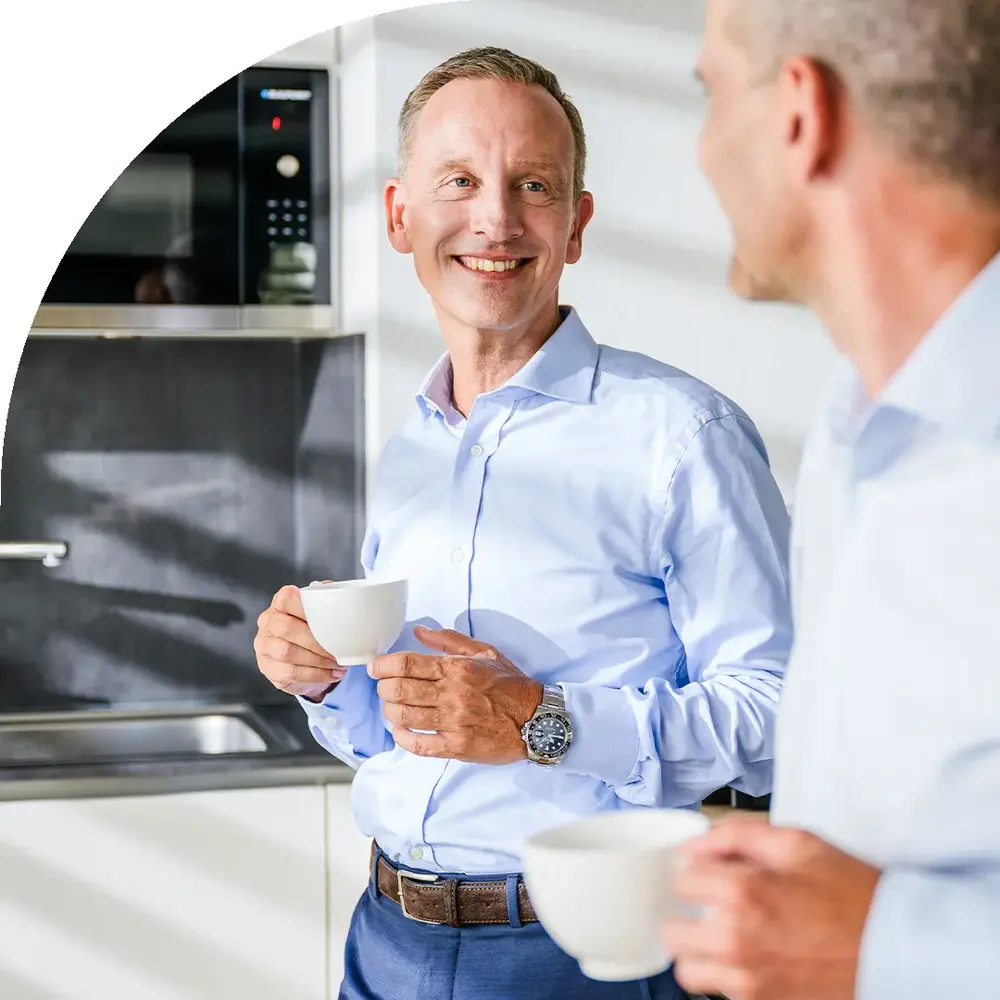 Zwei Männer in Hemden lächeln beim Kaffeetrinken in einer modernen Küche.