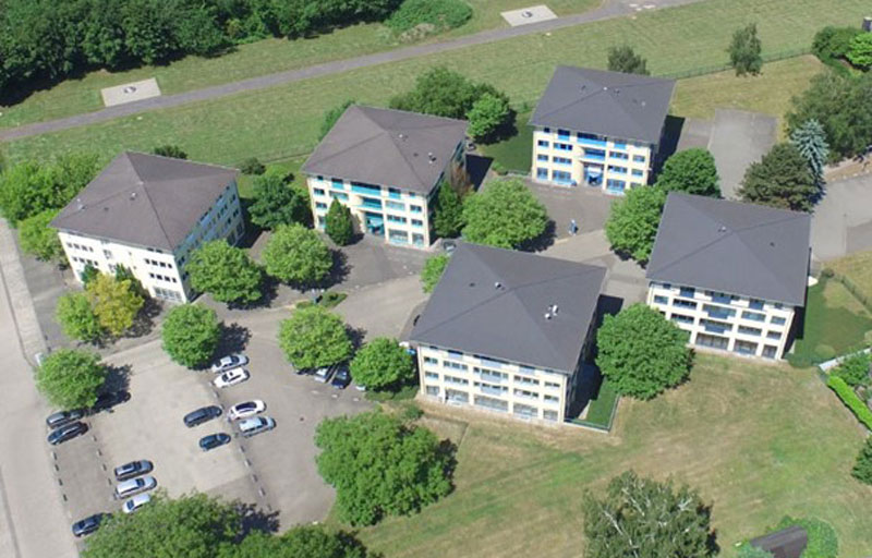 fünf Mehrfamilenhäuser aus der Vogelperspektive, Grünflächen rundherum, PKWs auf Parkplatz