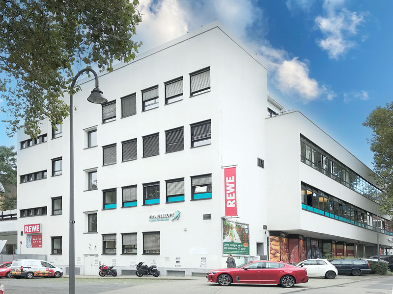 Großes weißes Gebäude mit Supermarkt im Erdgeschoss, blauer Himmel und Parkplätzen