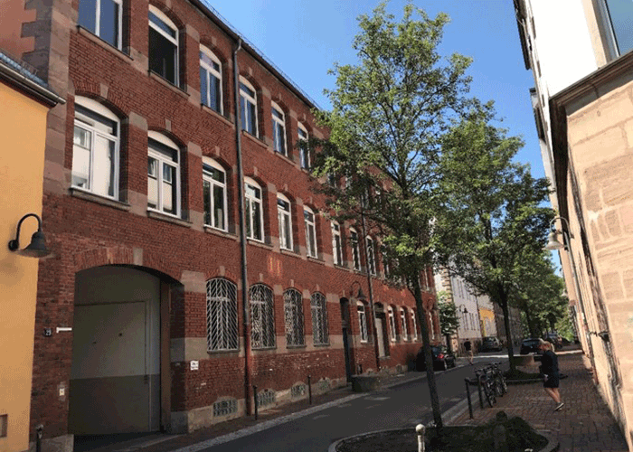 Rustikales Gebäude mit Einzelhandel im Erdgeschoss, Straßenbahnhaltestelle und Menschen
