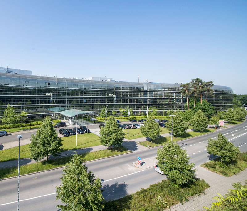 Modernes mehretagiges Gebäude mit Glassfassade, einer Straße und vielen Bäumen