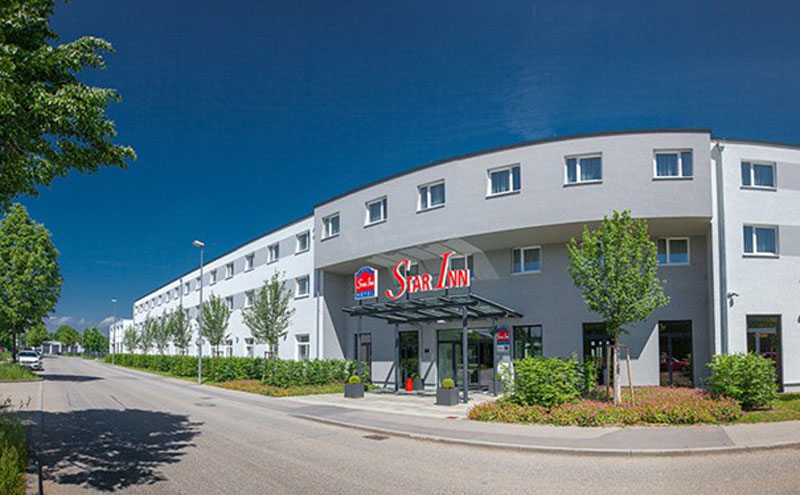 Drei Etagiges Gebäude mit jungen Bäumen und wenig befahrener Straße davor